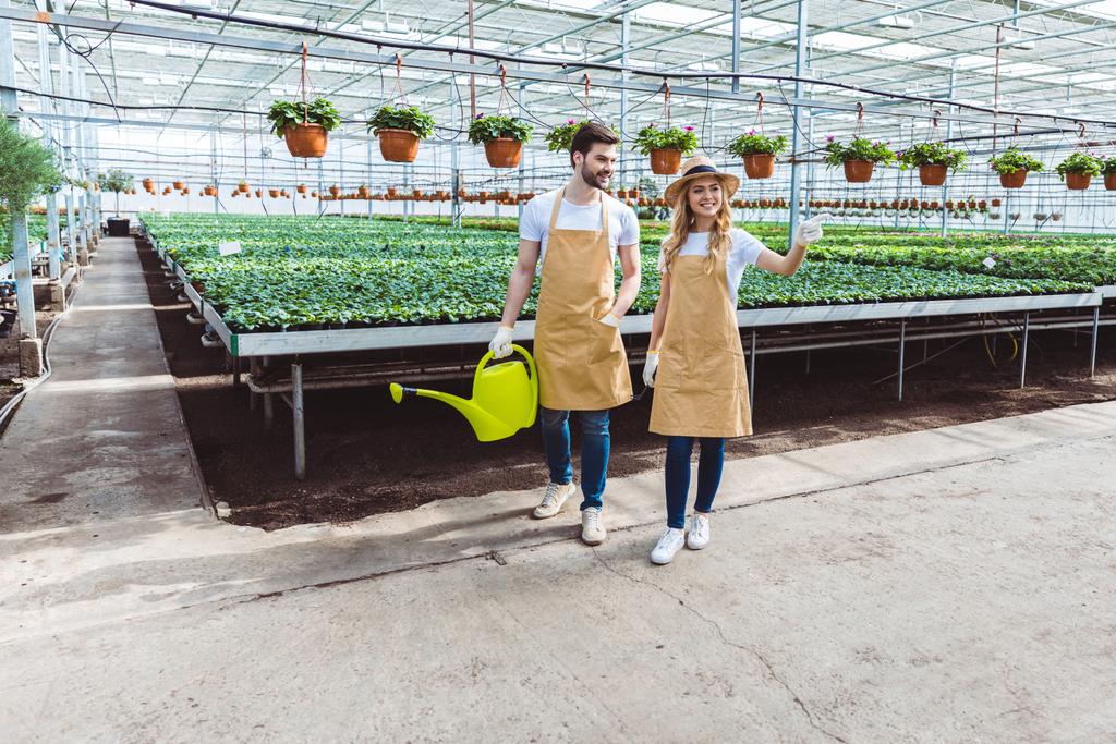 Mujer con rastrillo y hombre con regadera trabajando en invernadero
 - Foto, Imagen