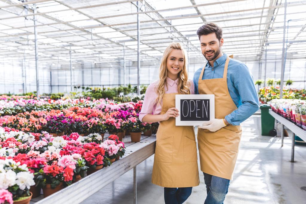 Male and female owners of glasshouse holding Open board by flowers - Photo, Image