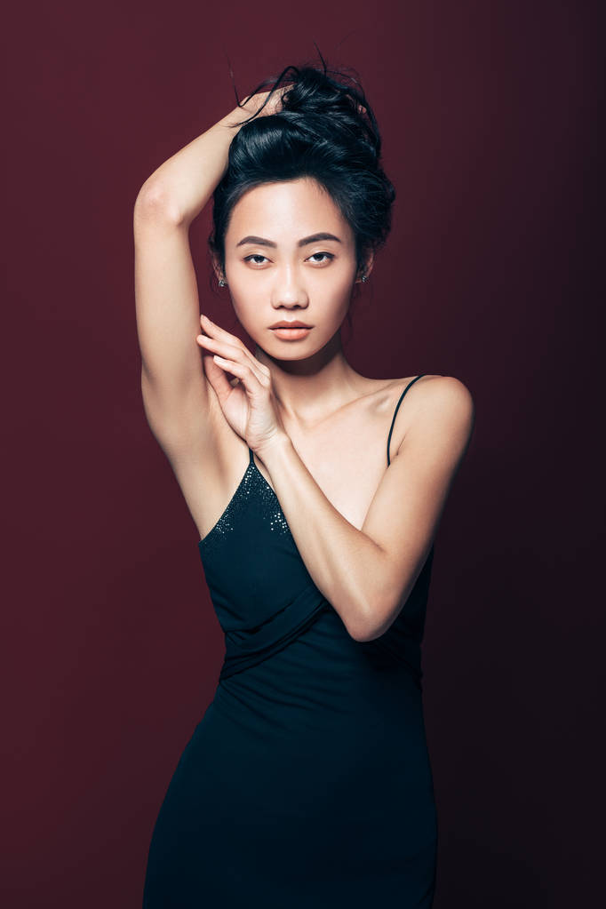 Mooie Aziatische vrouw in zwarte jurk poseren in studio op bruine achtergrond. Mooie fashion model portret - Foto, afbeelding