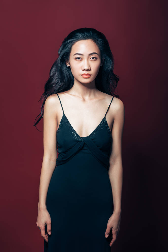 Красива азіатська жінка в чорному платті позує в студії на коричневому фоні. Портрет моделі моди
 - Фото, зображення