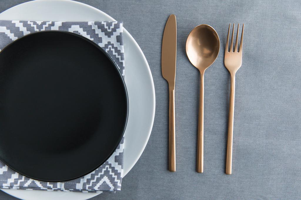 felülnézet asztallapra fekete üres lemez, szalvéta és régi vágású patinás evőeszközök - Fotó, kép