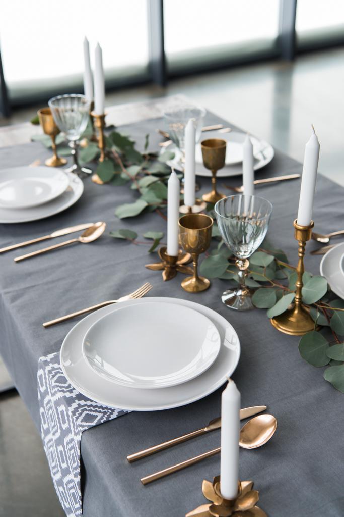 Nahaufnahme der rustikalen Tischdekoration mit Eukalyptus, Vintage-Besteck, Kerzen im Kerzenständer und leeren Tellern - Foto, Bild