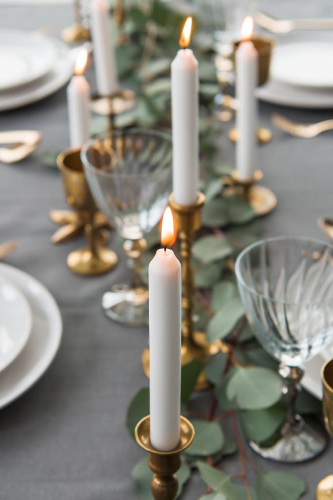 selektiver Schwerpunkt der rustikalen Tischdekoration mit Eukalyptus, altmodischem Besteck, Kerzen im Kerzenständer und leeren Tellern - Foto, Bild