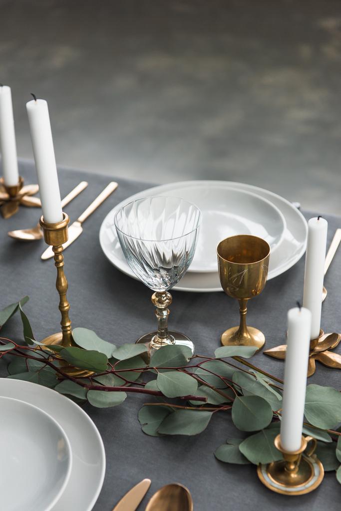 close up view of rustic table setting with wine glasses, eucalyptus, old fashioned cutlery, candles in candle holders and empty plates - Photo, Image