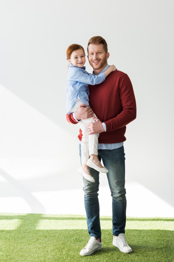 glücklicher Vater trägt entzückende kleine Tochter und lächelt in die Kamera auf grau - Foto, Bild
