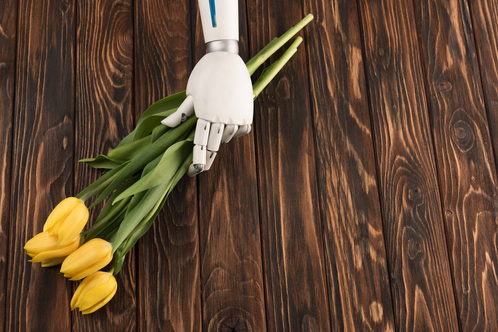 tiro recortado de robot sosteniendo hermoso ramo de tulipanes amarillos en la superficie de madera
 - Foto, Imagen