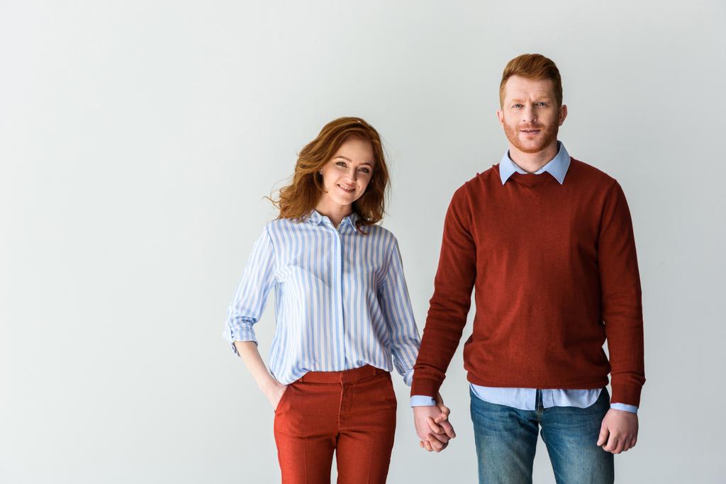 happy redhead couple holding hands and smiling at camera isolated on grey - Photo, Image