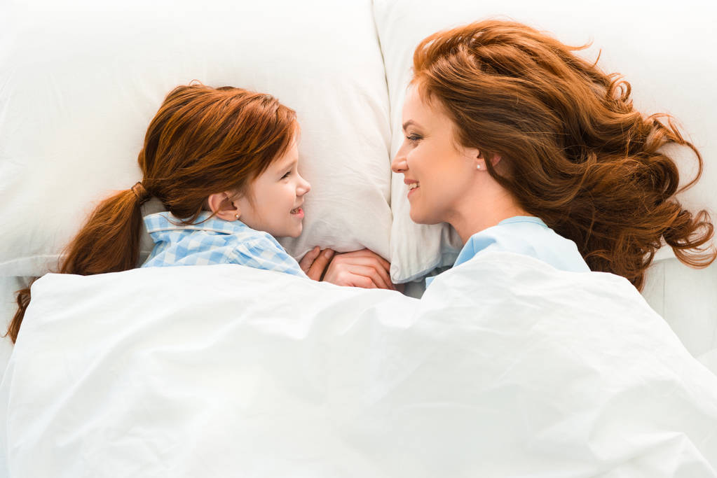 mooie roodharige moeder en dochter in bed liggen en glimlachen elkaar - Foto, afbeelding
