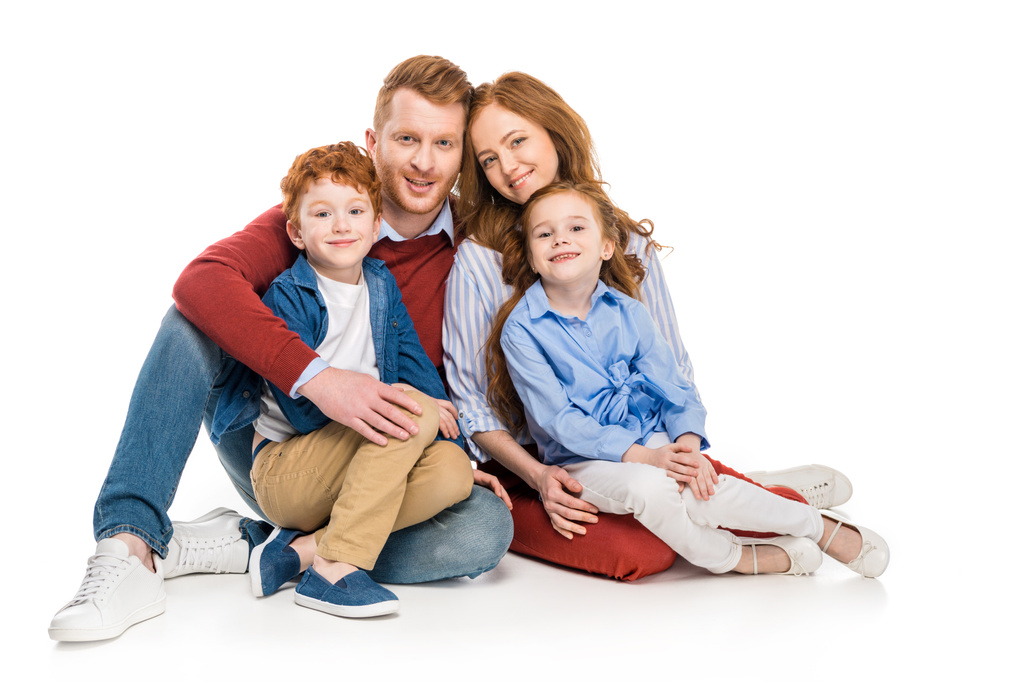 όμορφη κοκκινομάλλα ευτυχισμένη οικογένεια με δύο παιδιά κάθονται μαζί και να χαμογελά στη φωτογραφική μηχανή που απομονώνονται σε λευκό  - Φωτογραφία, εικόνα
