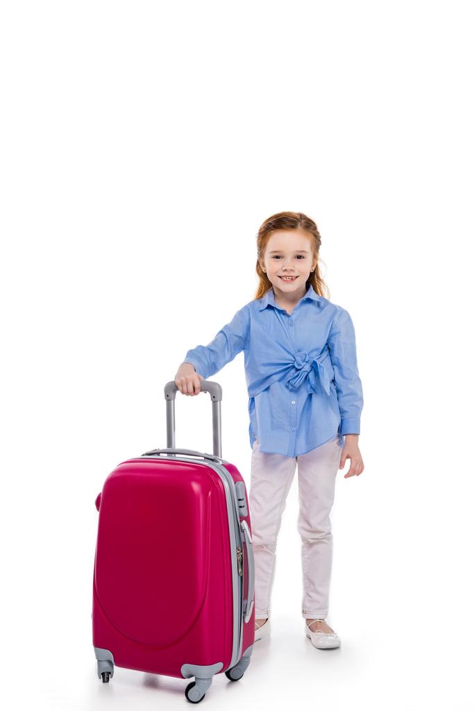 Niedliches kleines Kind steht mit Koffer und lächelt in die Kamera isoliert auf weiß - Foto, Bild