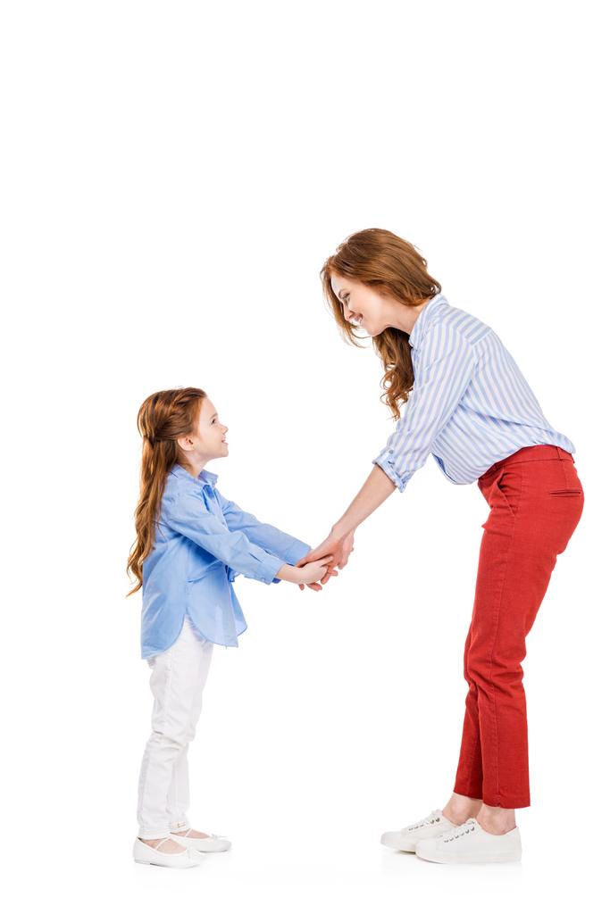 вид сбоку счастливой рыжеволосой матери и дочери, держащихся за руки и улыбающихся друг другу на белом фоне
 - Фото, изображение