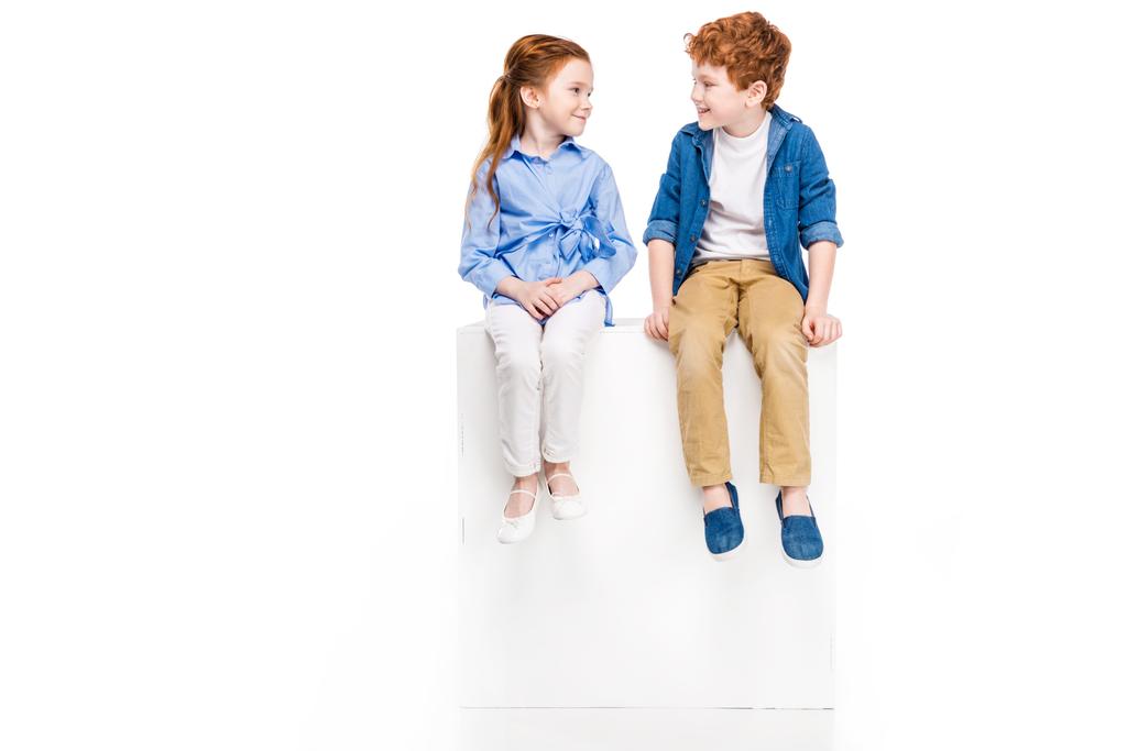 entzückende kleine Kinder sitzen auf weißen Würfeln und lächeln einander isoliert auf weißen Würfeln zu - Foto, Bild