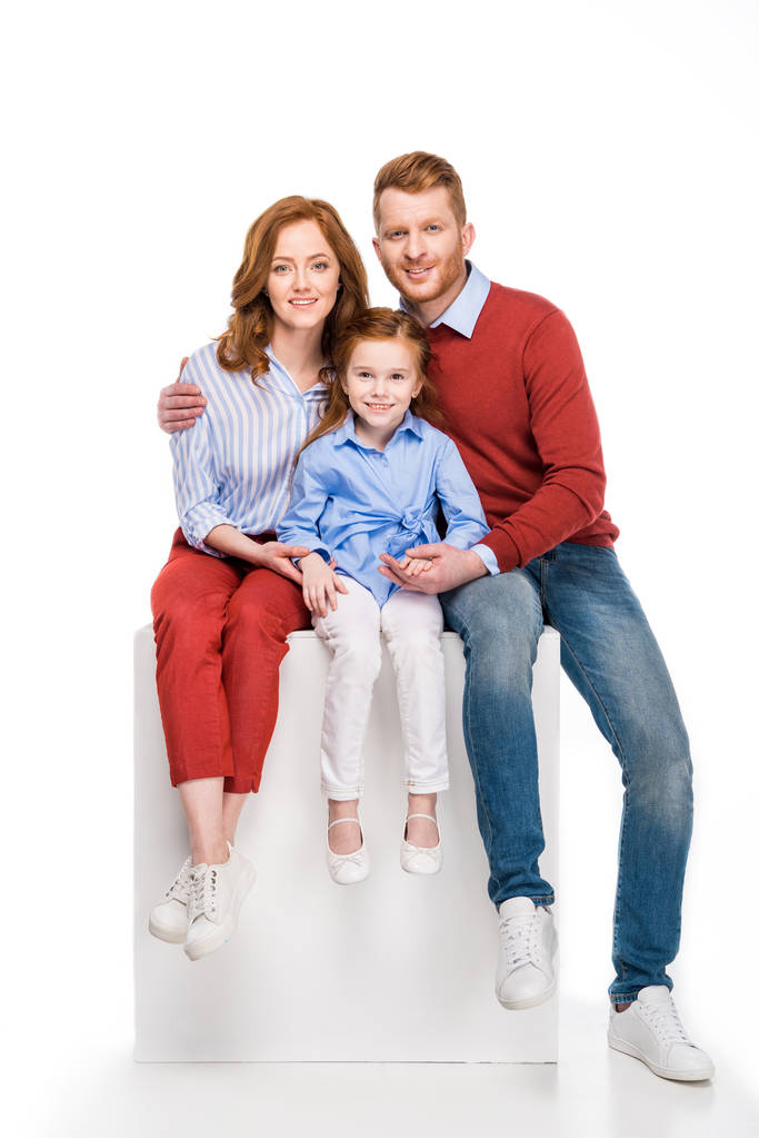 happy redhead family sitting on white cube and smiling at camera isolated on white - Photo, Image