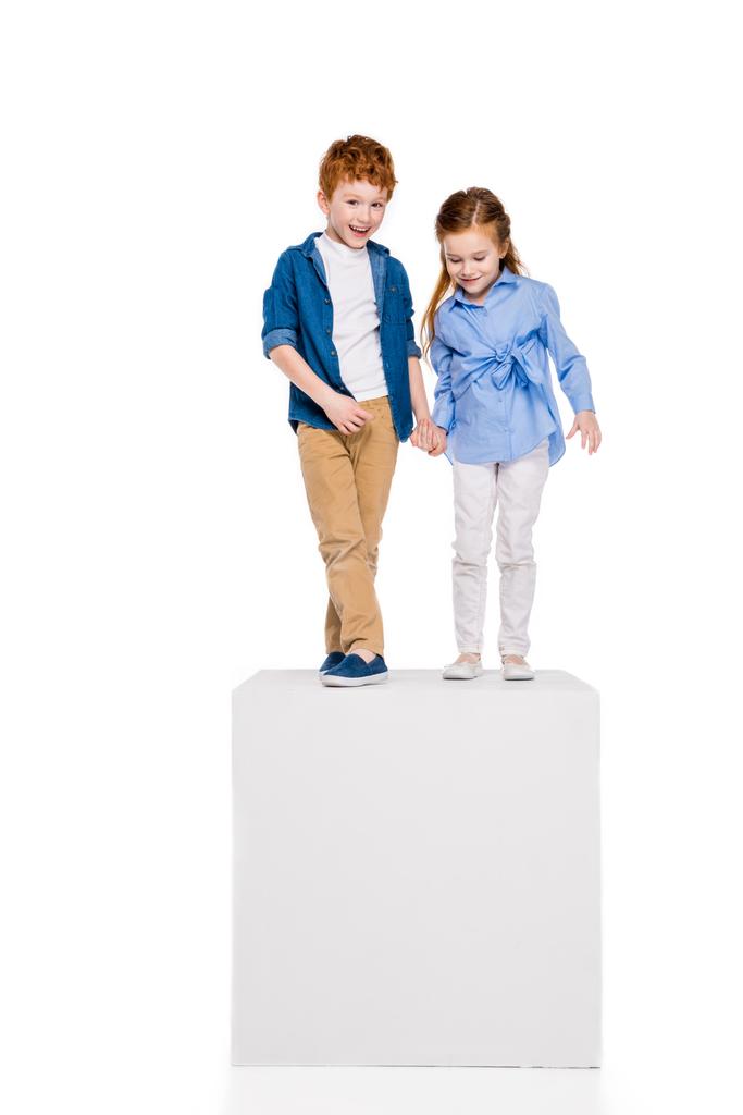 прелестные маленькие дети держась за руки и стоя на белом кубе изолированы на белом
 - Фото, изображение