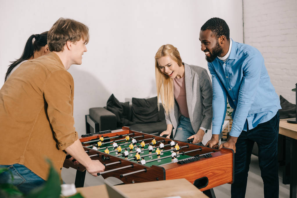 sonrientes colegas de negocios multiétnicos jugando futbolín en la oficina moderna
  - Foto, imagen