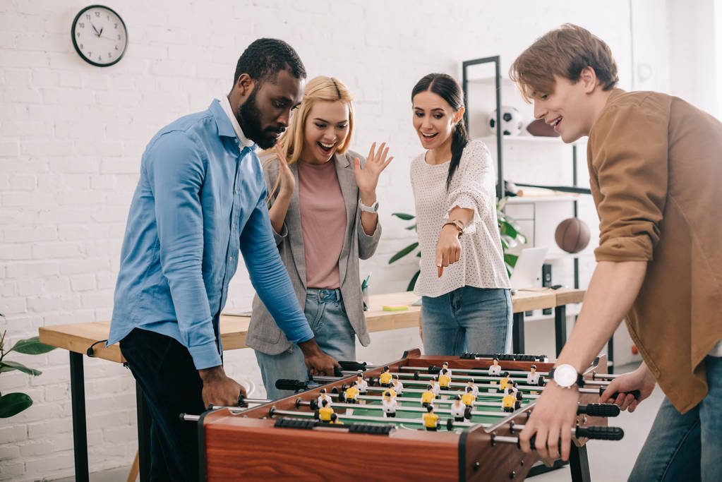 テーブル サッカー、ゲーム ボードを指す女性の同僚を再生多文化のビジネスマンの側面図 - 写真・画像