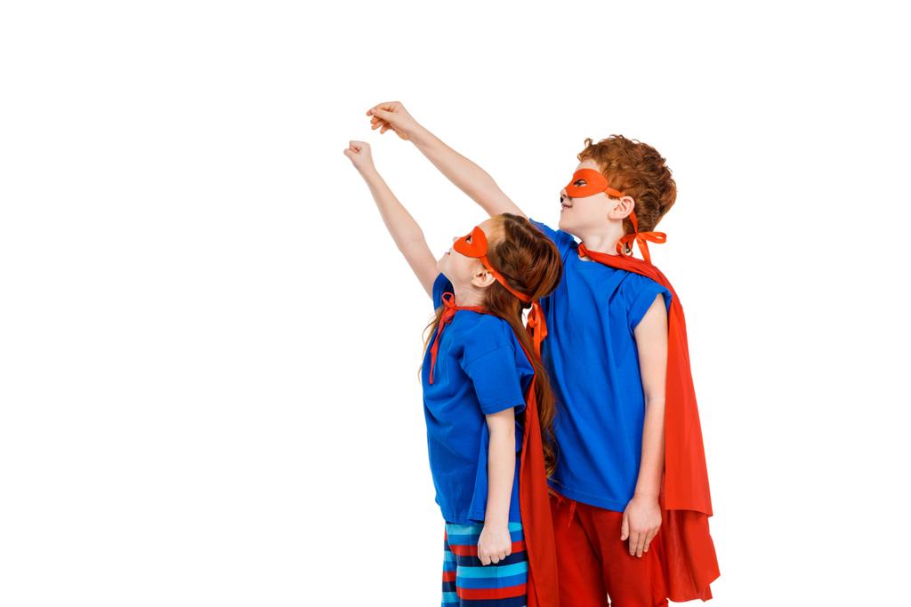 Super kinderen in maskers en mantels verhogen handen en op zoek weg geïsoleerd op wit - Foto, afbeelding