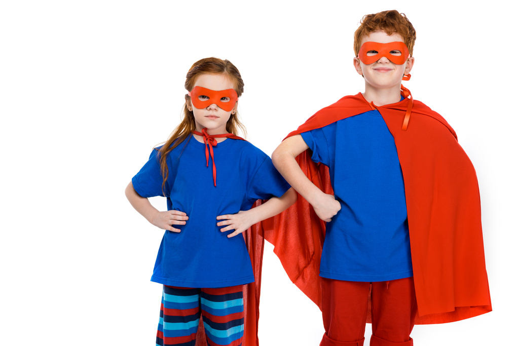 Superkinder in Masken und Mänteln stehen mit den Händen auf der Taille und schauen vereinzelt in die Kamera auf Weiß  - Foto, Bild