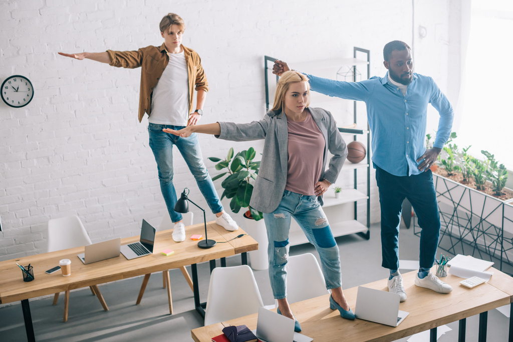 высокий угол обзора счастливых многонациональных деловых коллег, веселящихся и танцующих на столах в современном офисе
  - Фото, изображение