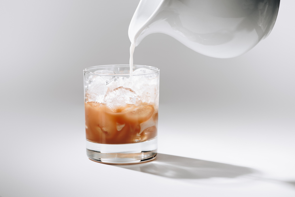 Zamknij widok mleko spływał do szklanki mrożonej kawy procesu na białym stole - Zdjęcie, obraz
