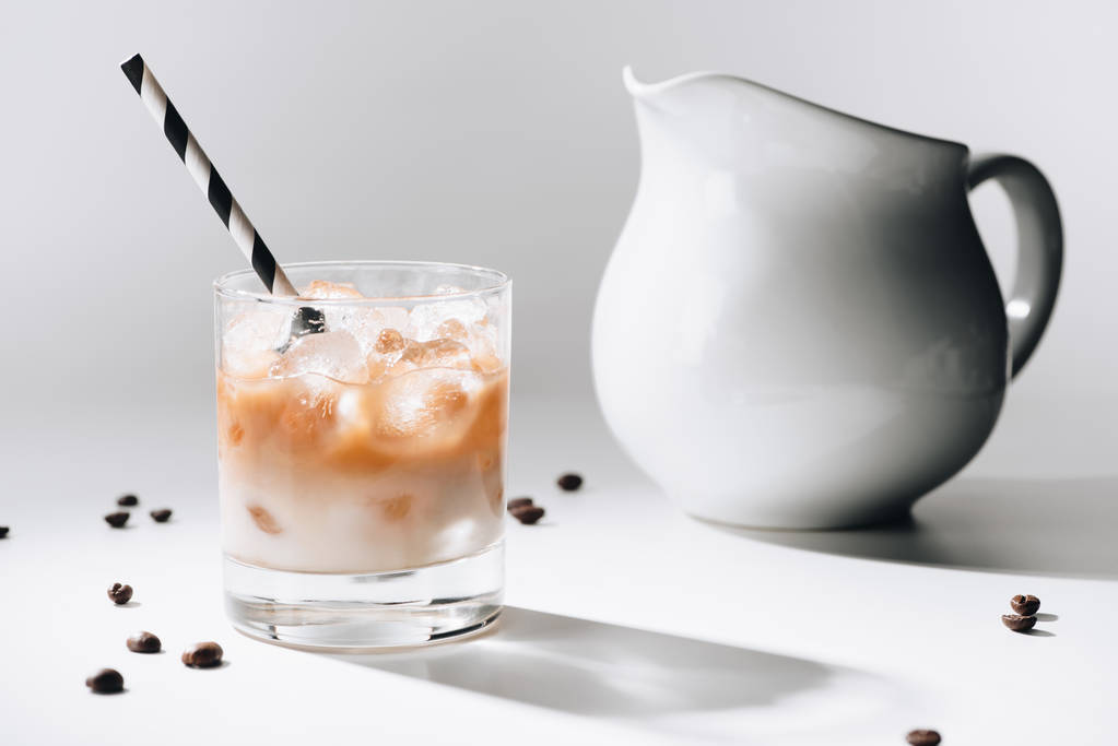 Close-up van jag van melk en glas koude koffie met stro op wit tafelblad - Foto, afbeelding