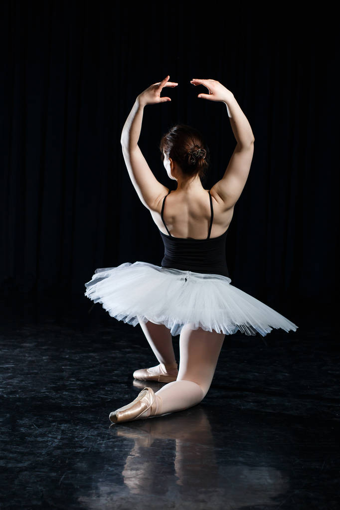 Mädchen Ballerina posiert und führt Tanzelemente in hellem szenischen Licht auf schwarzem Hintergrund vor - Foto, Bild