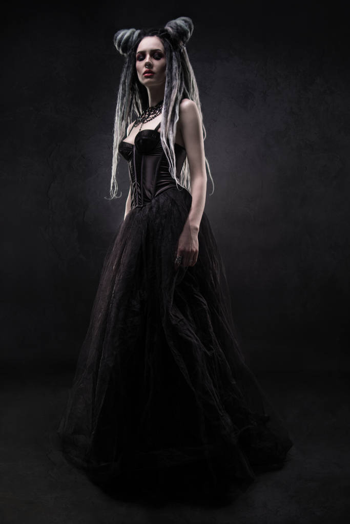 Mulher com dreads e vestido gótico preto posando no fundo escuro
 - Foto, Imagem