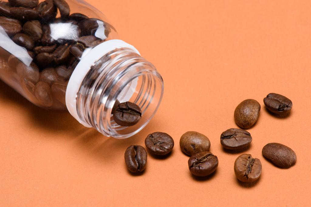 close up view of roasted coffee beans and plastic bottle isolated on peach - Photo, Image