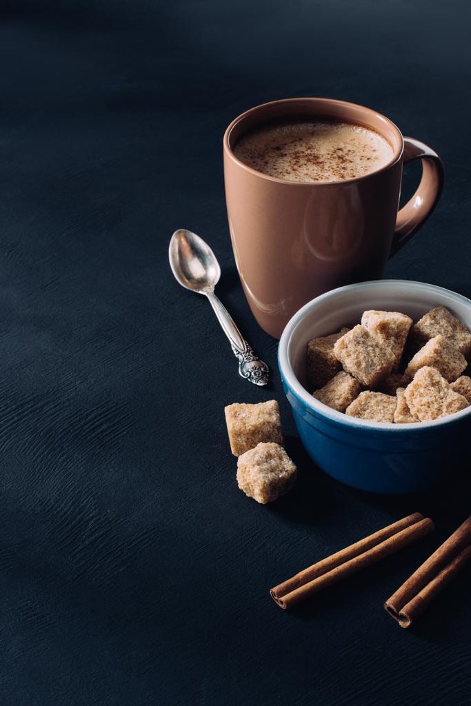 close up view of cup of coffee, bowl with brown sugar and cinnamon sticks on dark surface - Photo, Image