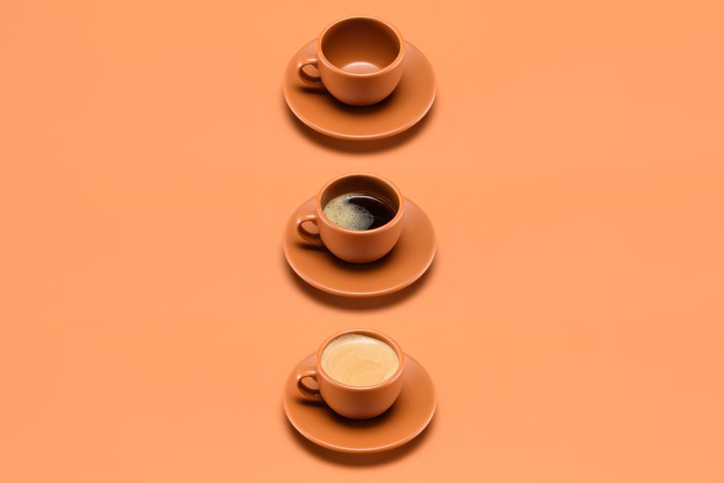 Close-up van plaatsing van lege cup en twee kopjes koffie geïsoleerd op perzik - Foto, afbeelding