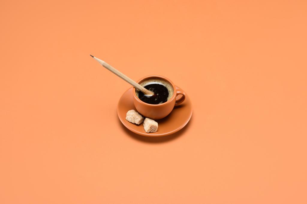 κλείνω πάνω θέα του καφέ με μολύβι και ζάχαρη από ζαχαροκάλαμο σε πιατάκι που απομονώνονται σε ροδάκινο - Φωτογραφία, εικόνα