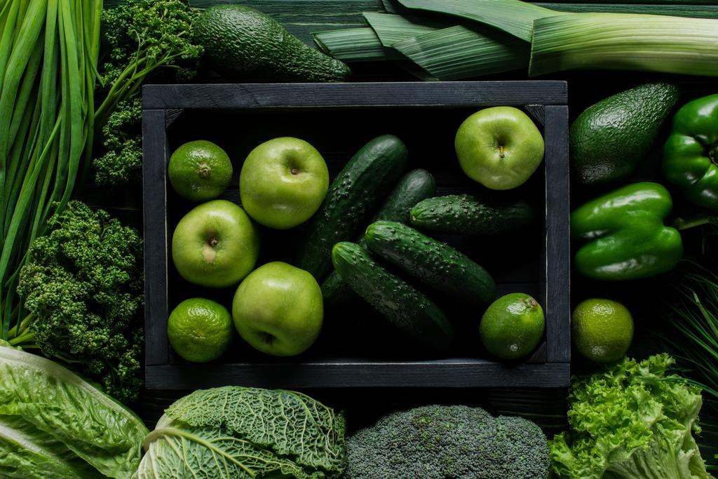 Äpfel und Gurken in Holzkiste zwischen grünem Gemüse, gesundes Ernährungskonzept - Foto, Bild