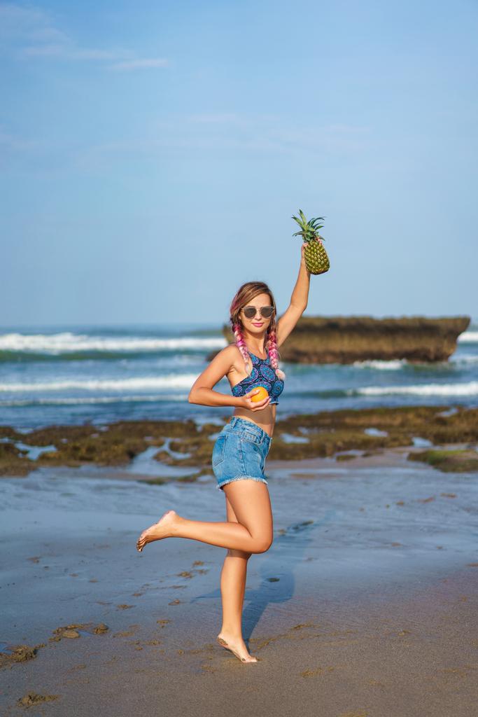 attraente giovane donna con arancia e ananas sulla spiaggia
 - Foto, immagini