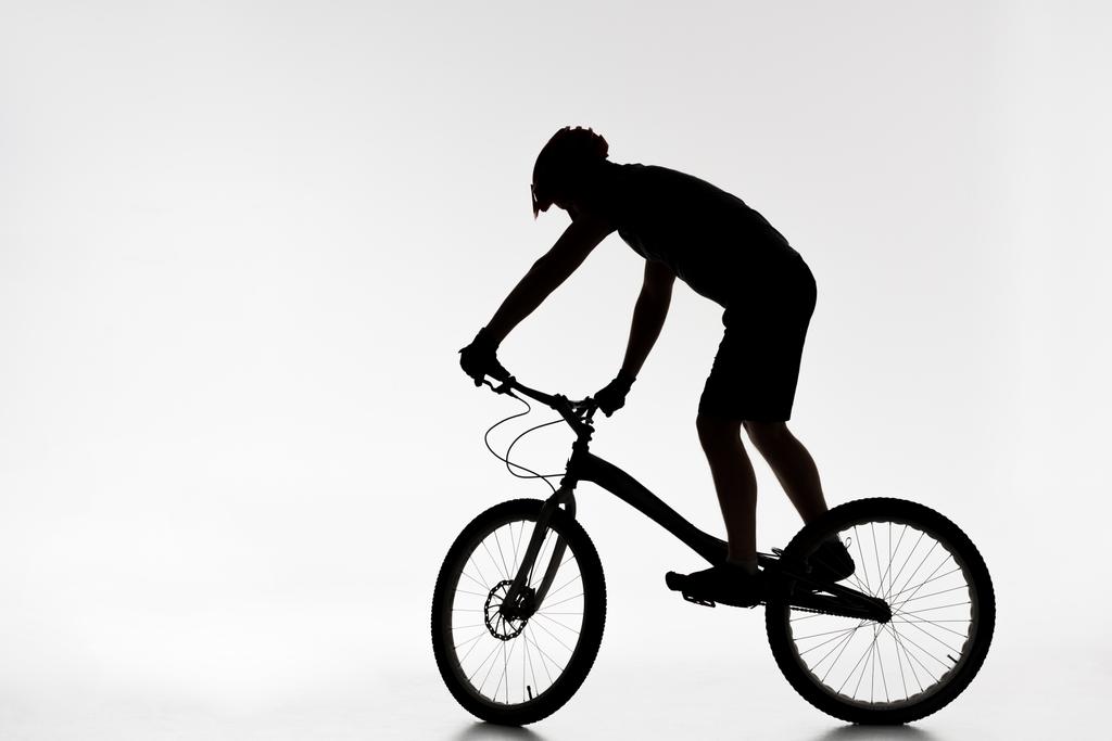 silhouet van proef biker in helm balanceren op fiets op wit - Foto, afbeelding