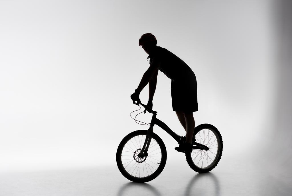 силуэт пробного велогонщика в шлеме, балансирующего на велосипеде на белом
 - Фото, изображение