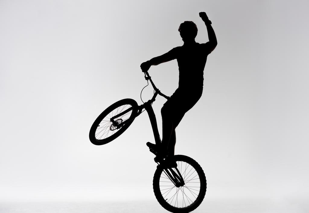σιλουέτα του δοκιμή ποδηλάτης έλεγχοι στέκεται στον πίσω τροχό και την αύξηση το χέρι σε λευκό - Φωτογραφία, εικόνα