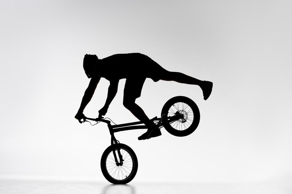 siluetti kokeiluversio biker suorittaa etupyörän tasapainotus temppu polkupyörän valkoinen
 - Valokuva, kuva