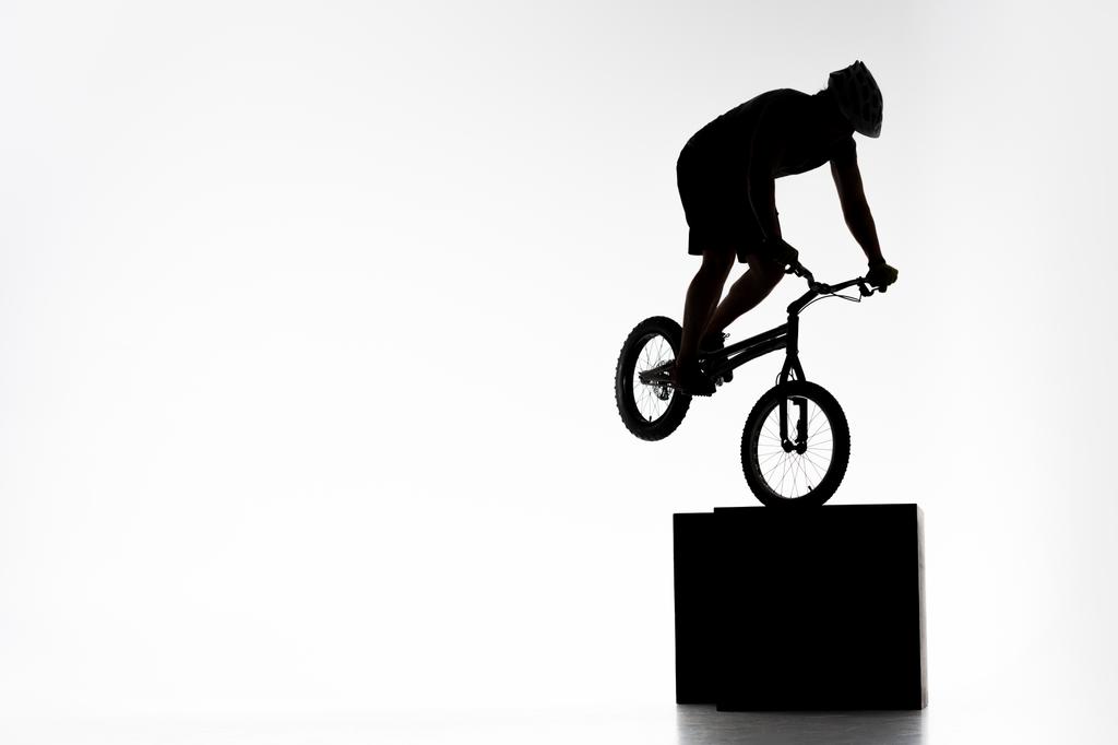 Silhouette eines Trial-Radfahrers beim Balancieren auf einem Würfel auf weißem Grund - Foto, Bild