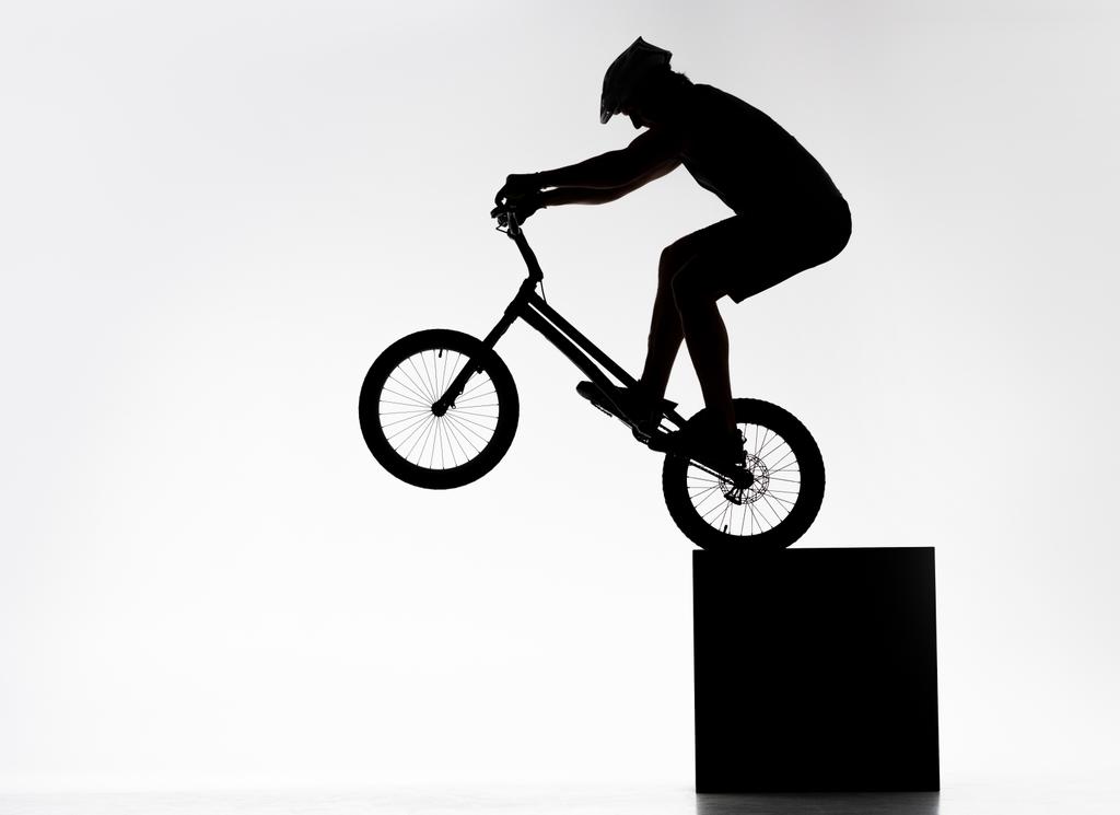 силуэт пробного велосипедиста, выполняющего задний стенд колеса, балансируя на кубе на белом
 - Фото, изображение