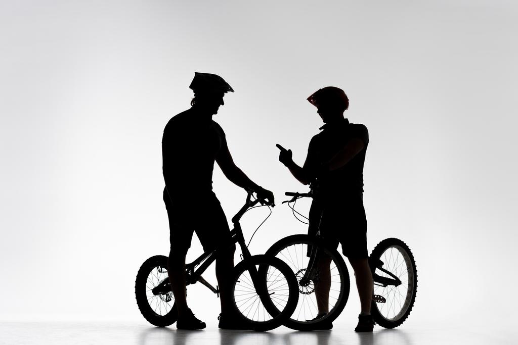 σιλουέτες των δίκη ποδηλάτες με ποδήλατα κουβεντιάζοντας σε λευκό - Φωτογραφία, εικόνα