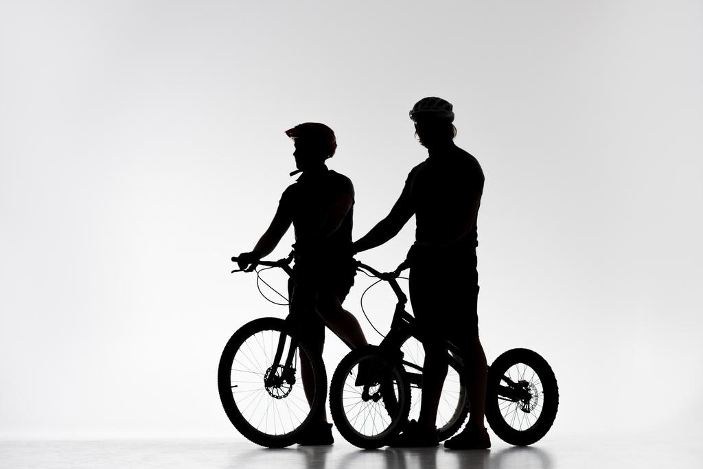 силуэты пробных байкеров в шлемах с велосипедами на белом
 - Фото, изображение