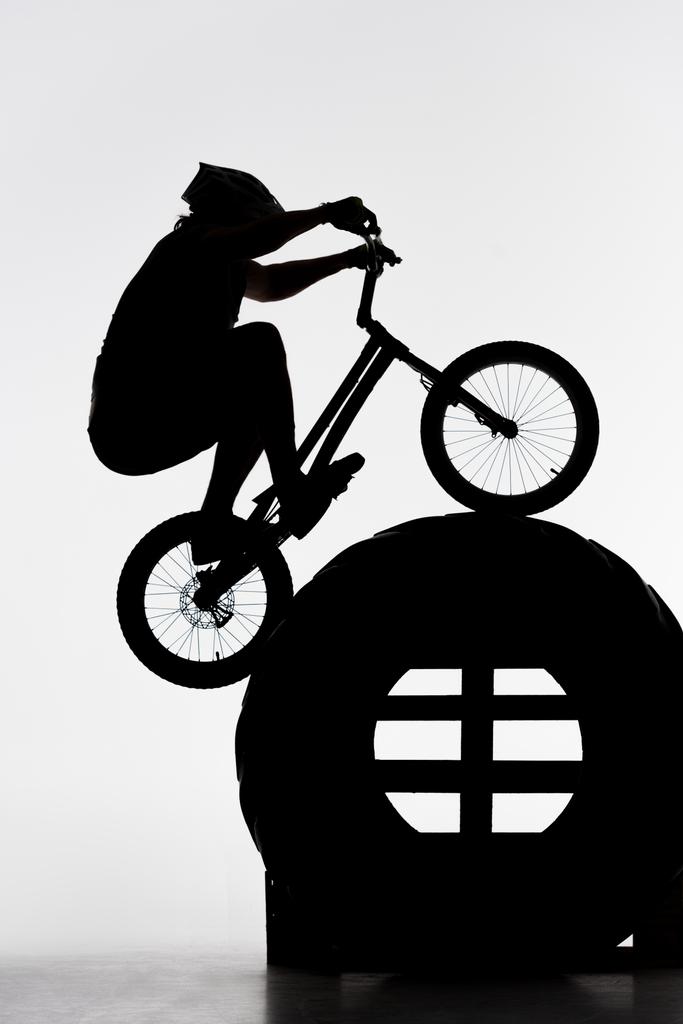 silhouette of trial biker jumping on tractor wheel on white - Photo, Image