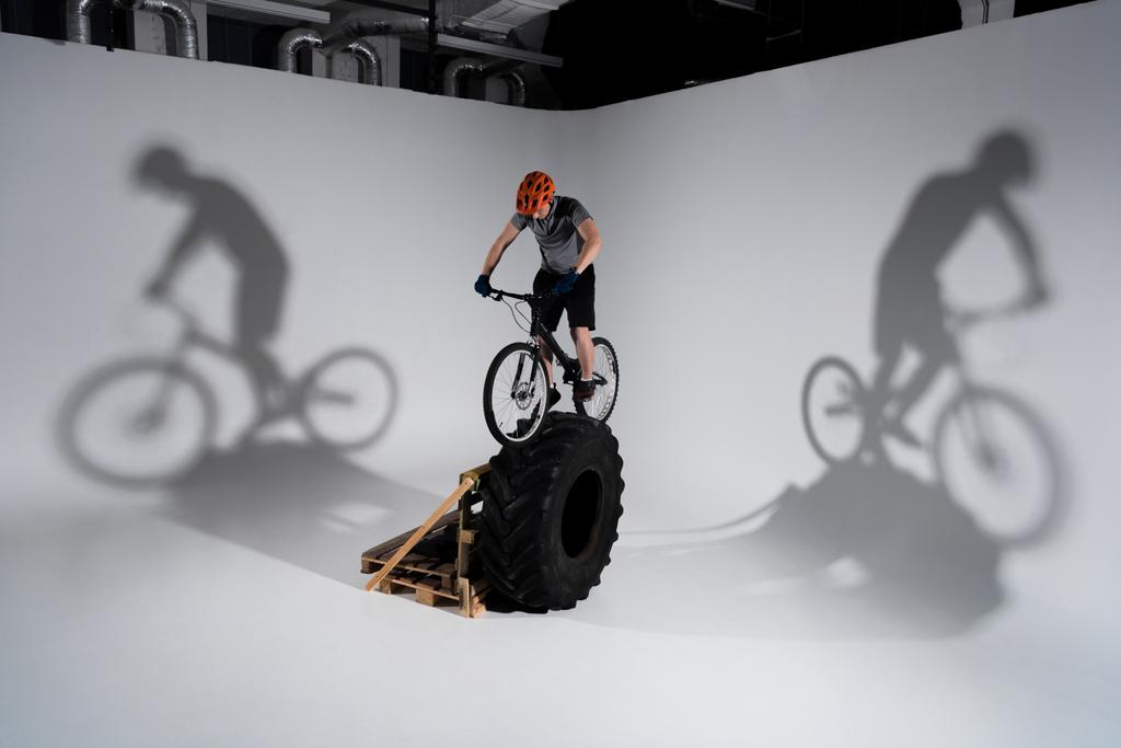 молодой опытный байкер в шлеме балансирует на колесе трактора
 - Фото, изображение
