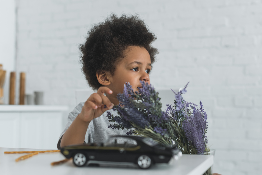 rozkošný chlapec afroamerické dotýká fialové květy a koukal doma - Fotografie, Obrázek