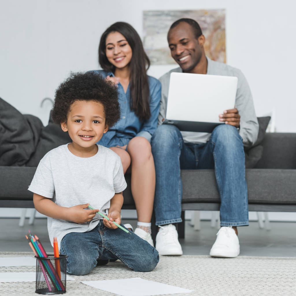 african american son looking at camera while drawing on floor at home - Photo, Image