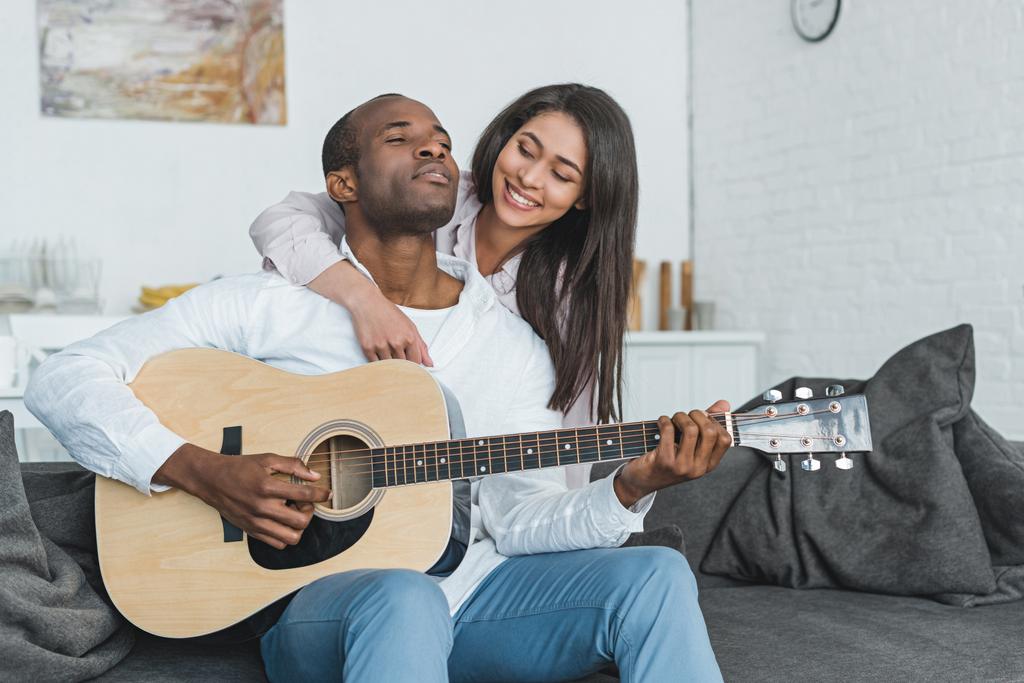 novio afroamericano tocando la guitarra para la novia feliz en casa
 - Foto, imagen