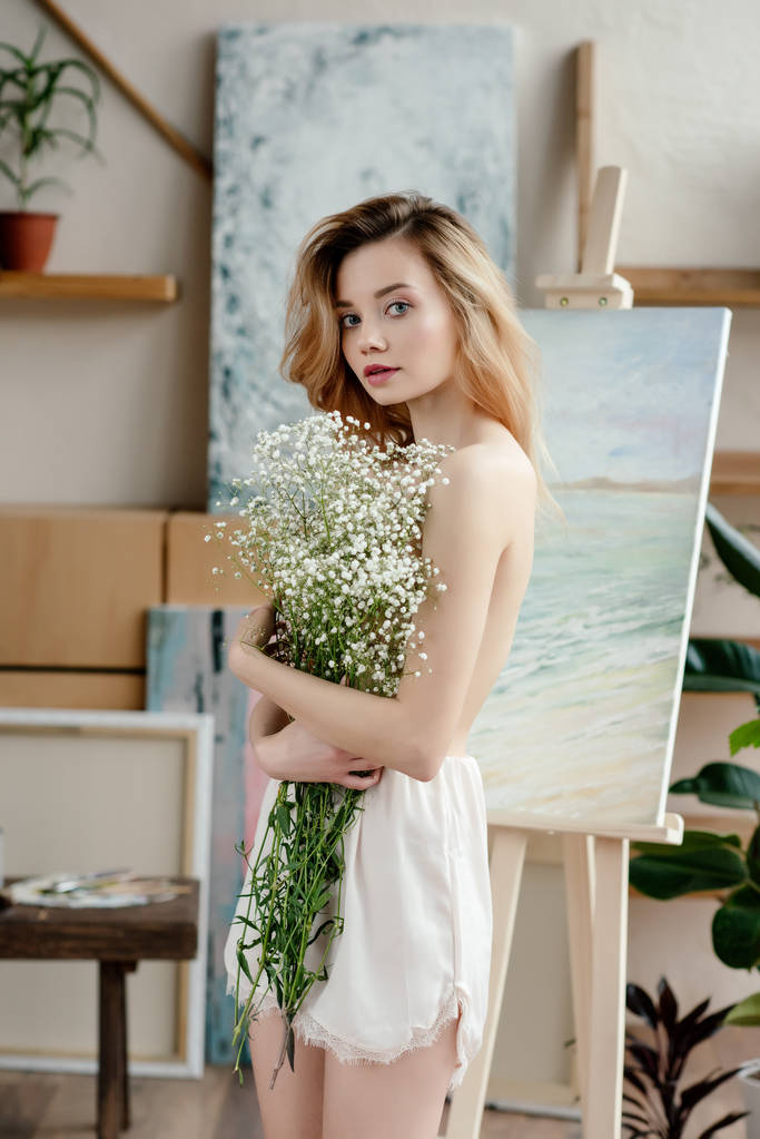 piękna młoda kobieta nagi gospodarstwa kwiaty białe i patrząc na kamery w studio sztuki   - Zdjęcie, obraz