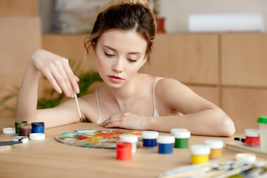 belle jeune peintre femme tenant pinceau et regardant la palette dans l'atelier d'art
  - Photo, image