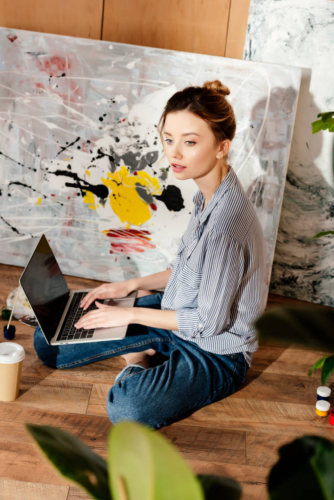 όμορφη νεαρή γυναίκα καλλιτέχνης χρήση φορητού υπολογιστή με κενή οθόνη στο studio - Φωτογραφία, εικόνα
