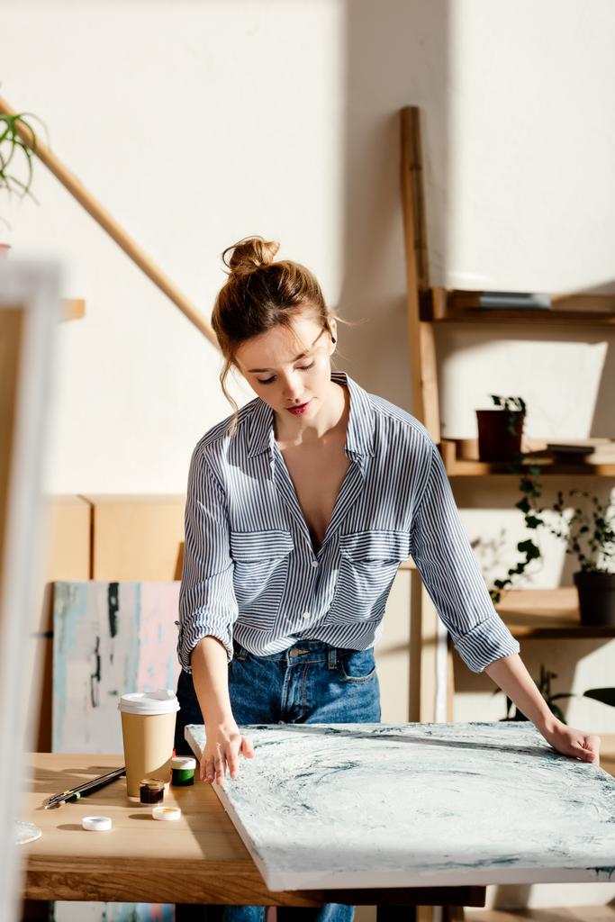 female artist looking at own painting on table with coffee cup  - Photo, Image